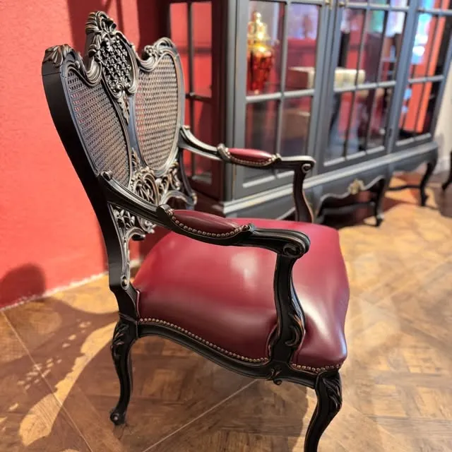 A carved chair with a cane back and a red leather seat.